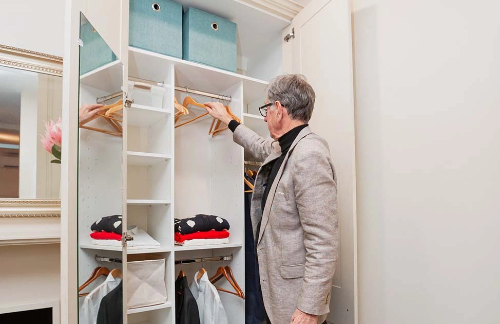 A man stands in front of a closet, browsing through different clothes and deciding what to wear