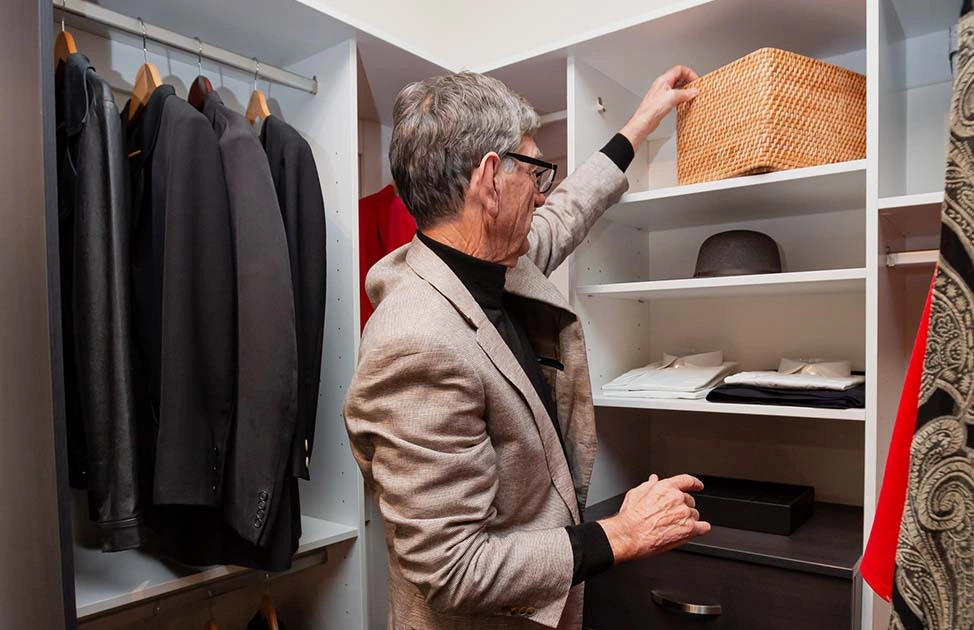 A man is arranging clothes inside a closet, ensuring everything is in its place